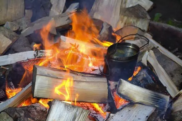 Kleine Flamme brennt zwischen Holzscheiten, Kessel hängt über dem Feuer