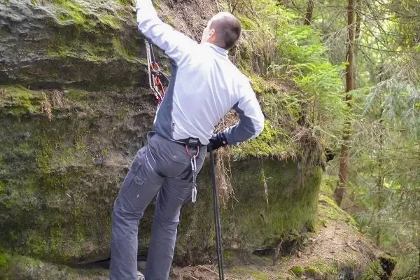 Kletterer sichert sich mit Karabiner an einer Felswand im Wald
