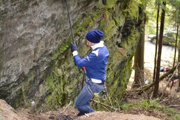 Kletterer sichert sich mit Seil an einer Felswand im Wald