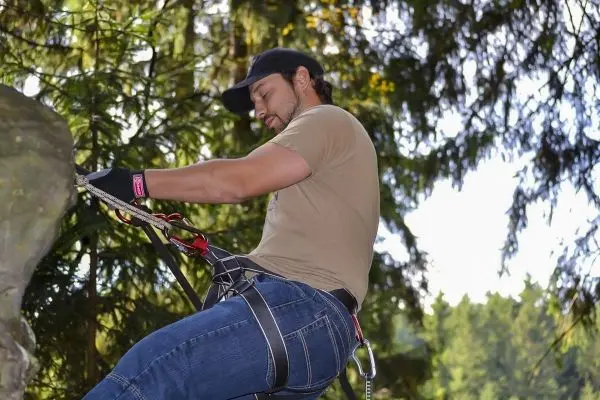 Kletterer sichert sich mit Seil und Karabiner an einem Baum