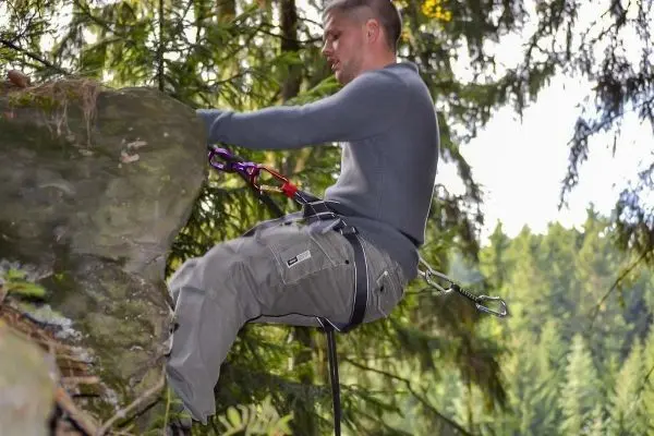 Kletterer sitzt an einem Felsvorsprung mit Sicherungsgerät und Karabiner