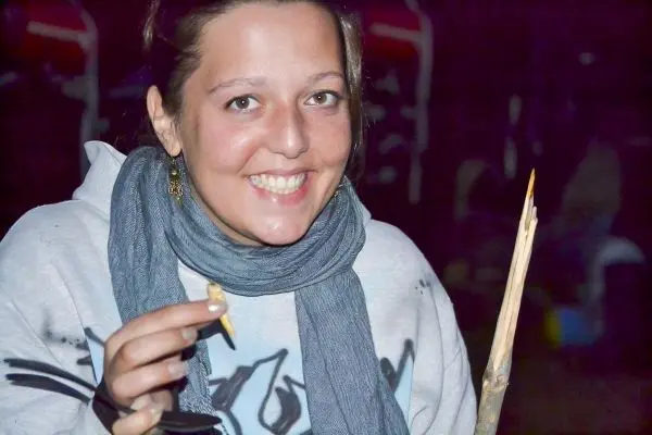 Lange Holzspitze in einer Hand, lächelt und hält einen kleinen Gegenstand