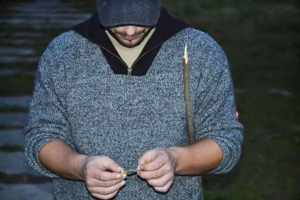 Mann bearbeitet Zunder mit zwei Händen und hält einen Stock in der anderen Hand