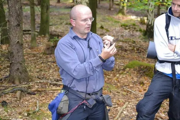 Mann erklärt eine Technik im Wald, hält ein Werkzeug in der Hand