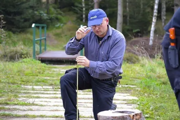 Mann kniet und misst mit einem Stock auf einem Waldweg