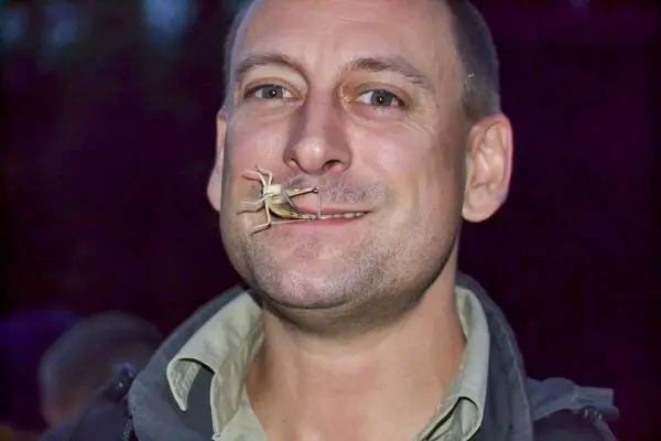 Mann mit Heuschrecke im Mund lächelt in die Kamera