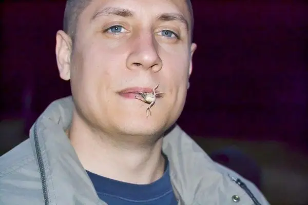 Mann mit Insekt im Mundbereich, trägt eine Jacke und schaut in die Kamera