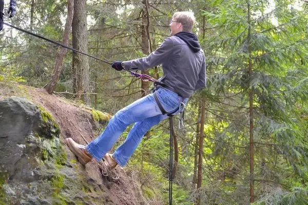 Mann seilt an einem Felsvorsprung mit Sicherungsseil und Kletterausrüstung