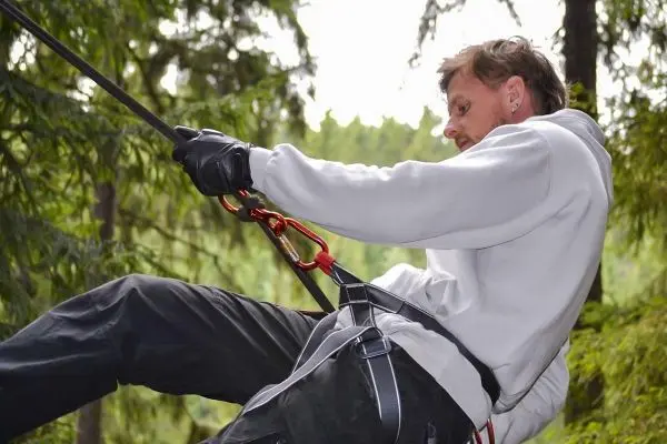 Mann sichert sich mit Karabiner und Seil beim Abseilen in den Wald