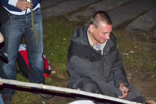 Mann sitzt am Boden und hält einen Stock in der Hand