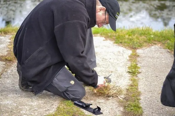 Messer schneidet Gras auf einem Gehweg neben einem Gewässer