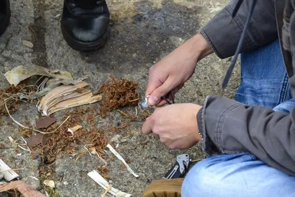 Person bearbeitet Zunder mit einem Messer auf dem Boden beim Survival Training