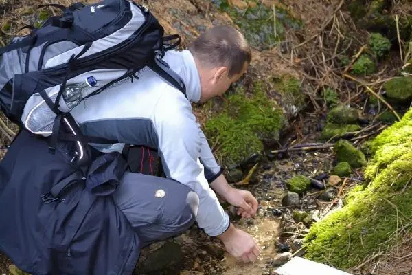 Person beugt sich über einen kleinen Bach und untersucht das Wasser