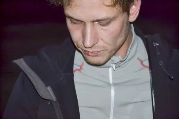 Person mit gesenktem Blick trägt sportliche Kleidung und steht in dunkler Umgebung