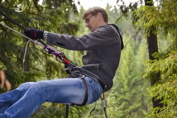 Person nutzt Seiltechnik zum Abseilen zwischen Bäumen