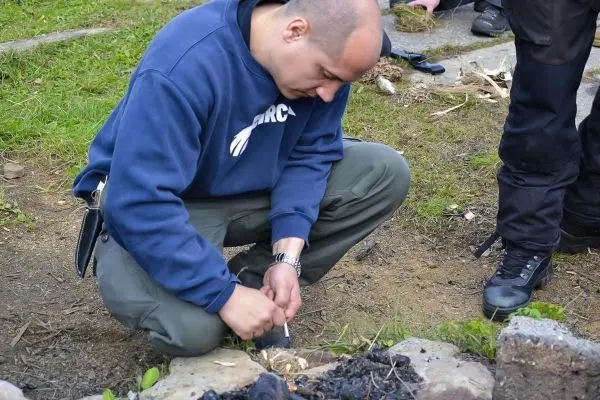 Person schnitzt mit einem Messer an einem Holzstück beim Überlebenstraining