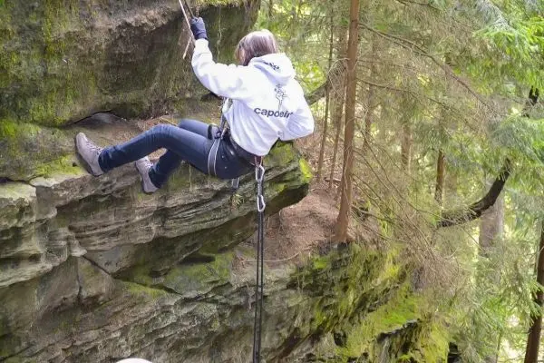 Person seilt an einer Felswand ab im Wald