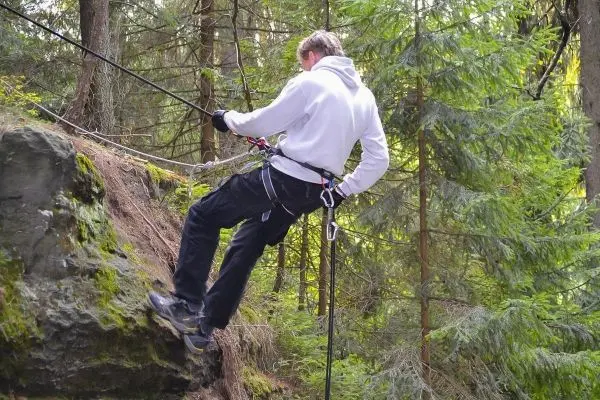 Person seilt an einer Felswand ab im Wald