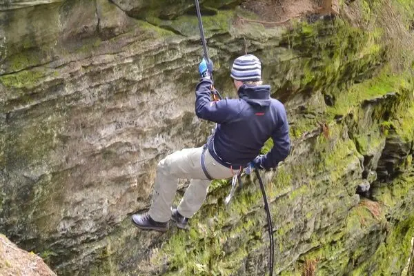 Person seilt an einer Felswand mit Seil und Kletterausrüstung ab