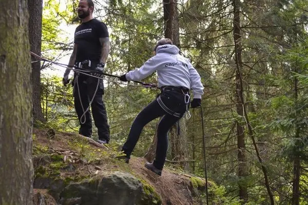 Person sichert sich beim Abseilen an einem Baum