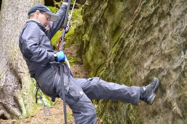Person sichert sich beim Abseilen an einer Felswand mit Seil und Karabiner