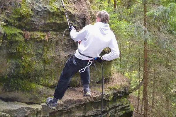 Person sichert sich mit Seil an einer Felswand im Wald