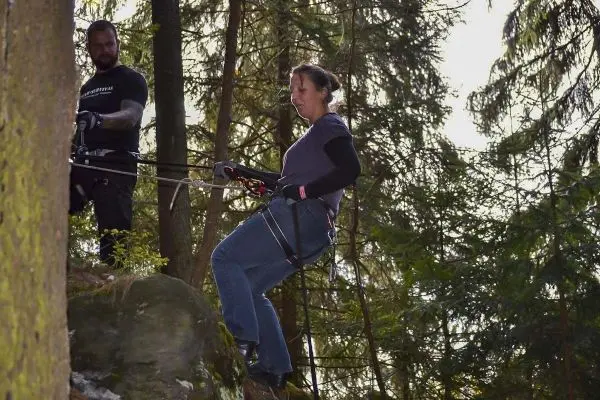 Person steht an einer Felswand und sichert sich beim Abseilen im Wald