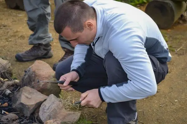 Person zündet mit einem Feuerstein trockenes Gras an