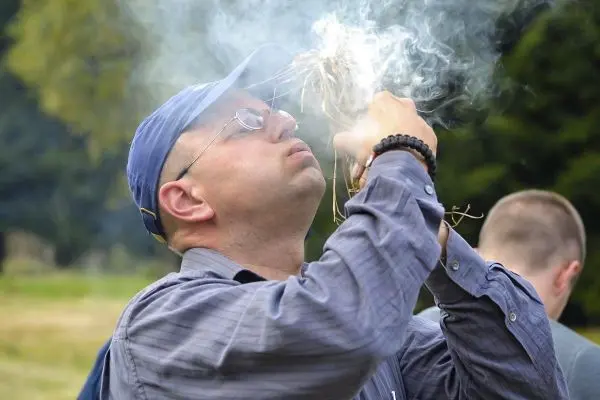 Zunder glimmt und raucht in den Händen, während er bläst