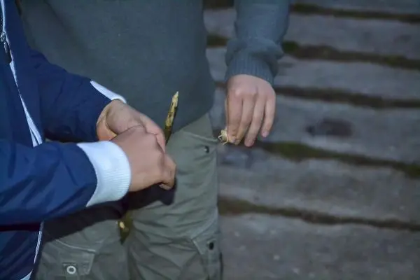 Zwei Hände halten einen Stock und ein Stück Holz zum Zundern