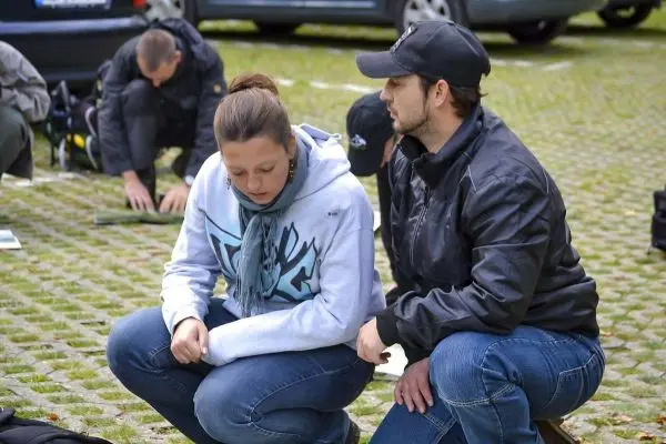 Zwei Personen sitzen auf dem Boden und betrachten Materialien, im Hintergrund weitere Teilnehmer