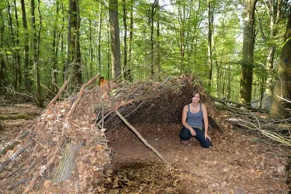 Biwak aus Ästen und Laub im Wald, Person sitzt davor