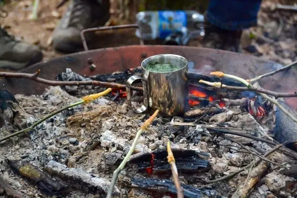 Edelstahlbecher steht über glühenden Kohlen in einem Feuerkreis