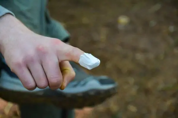 Finger mit Verband zeigt auf den Boden, Schuh im Hintergrund