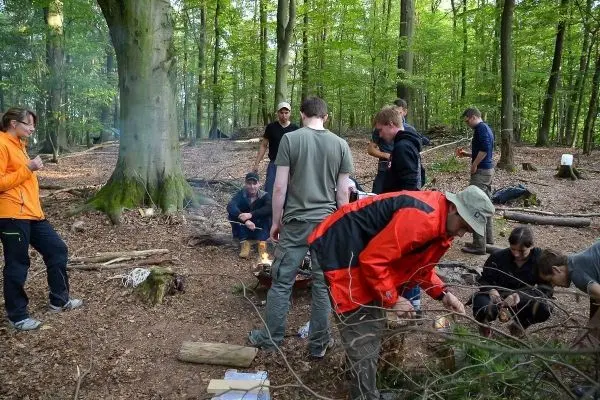Gruppe arbeitet am Lagerfeuer, Holz wird vorbereitet und Zunder gesammelt