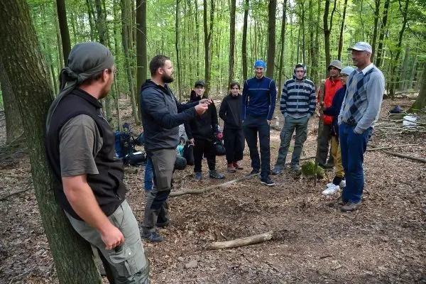 Gruppe diskutiert im Wald über Überlebenstechniken und Holzarbeit