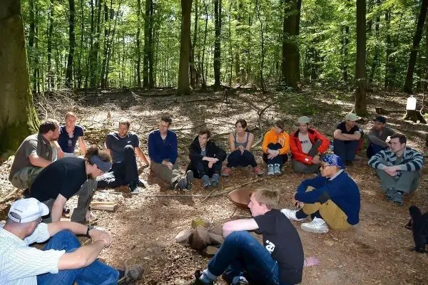 Gruppe sitzt im Wald um ein Lagerfeuer und beobachtet eine Demonstration