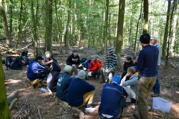 Gruppe sitzt im Wald und diskutiert gemeinsam beim Überlebenstraining