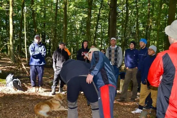 Gruppe von Personen beobachtet eine Demonstration im Wald, ein Hund liegt entspannt am Boden
