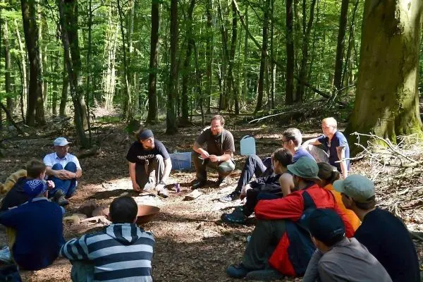 Gruppendiskussion im Wald, Teilnehmer sitzen um ein Feuerstelle