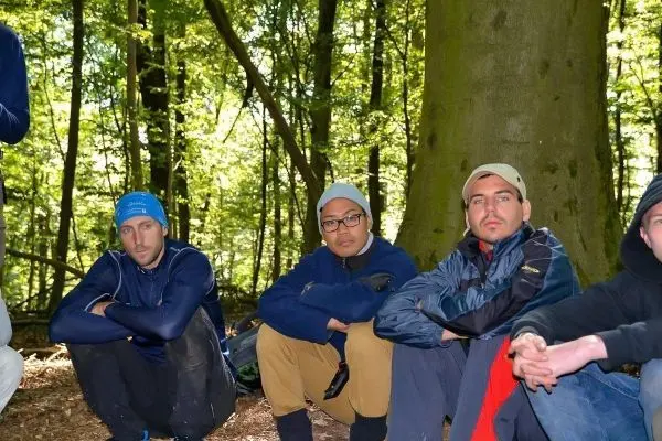 Gruppierung von Personen sitzt im Wald auf dem Boden, umgeben von Bäumen
