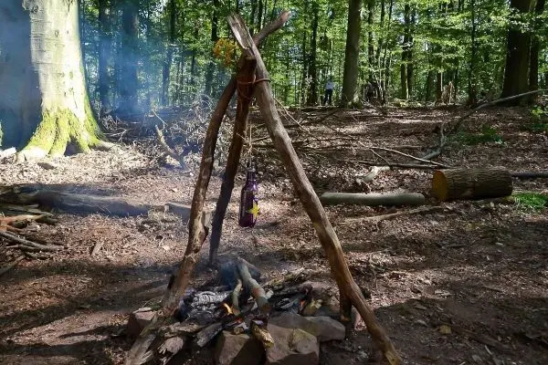 Hobo-Kocher mit Kessel über Feuerstelle, Rauch steigt auf