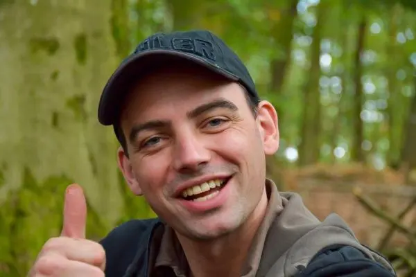 Lächelnde Person mit Daumen hoch in einem Waldgebiet