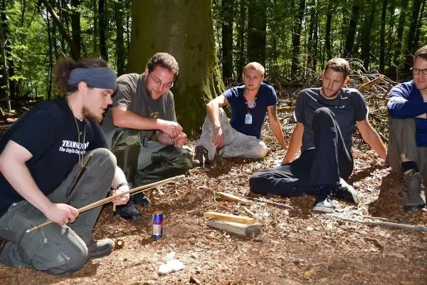 Mann demonstriert Feuerbohren mit einem Stock auf dem Waldboden