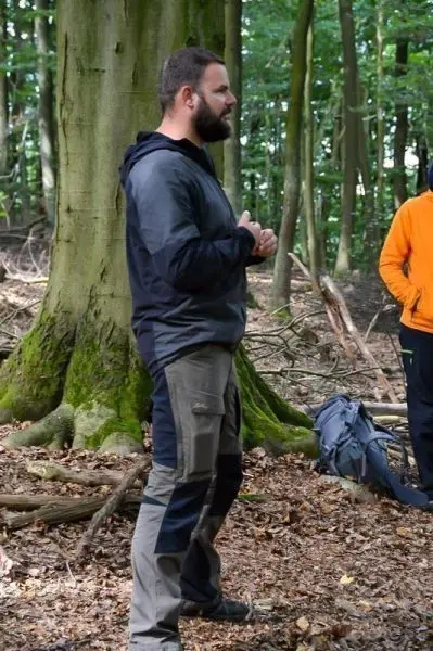 Mann steht neben einem Baum im Wald und spricht mit einer anderen Person