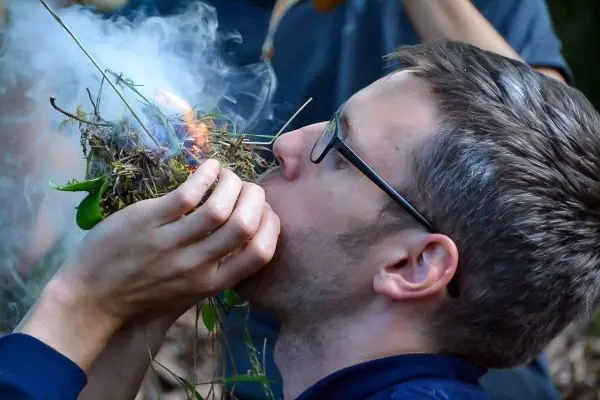 Person bläst in ein Nest aus Gras und Blättern