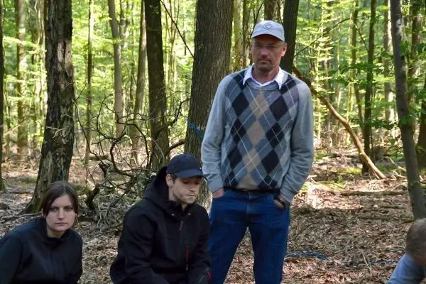 Person steht zwischen baeumen und beobachtet andere personen