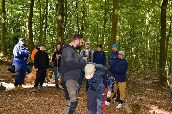 Person zeigt einer anderen Person eine Technik im Wald