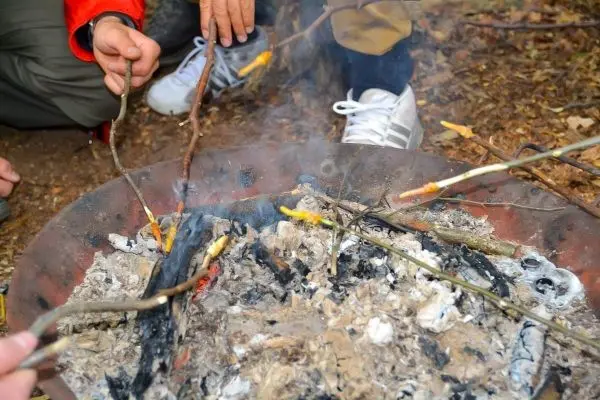 Zunder glimmt in einer Feuerstelle, während Äste darüber gehalten werden