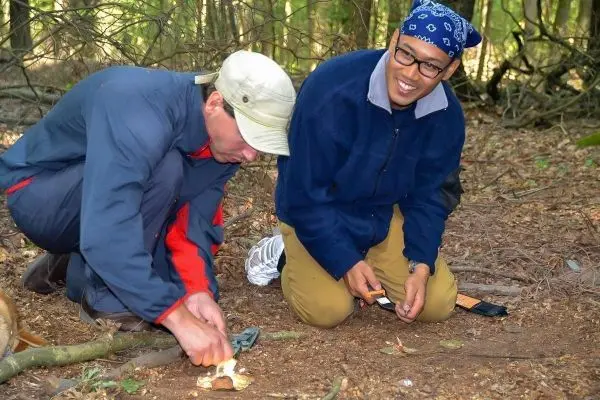 Zunder wird mit einem Messer bearbeitet, während ein anderer zuschaut